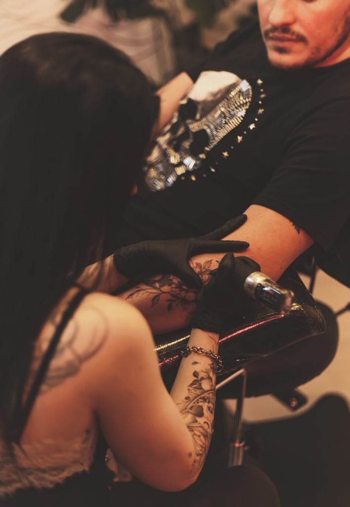 Pessoa fazendo uma tatuagem detalhada em estúdio de tattoo, destacando máquina de tatuagem e tinta preta.