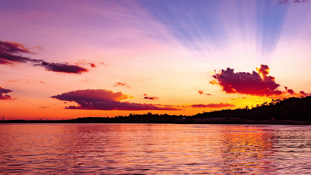 Pôr do sol deslumbrante sobre o mar com céu em tons de rosa e laranja, refletindo na água tranquila.