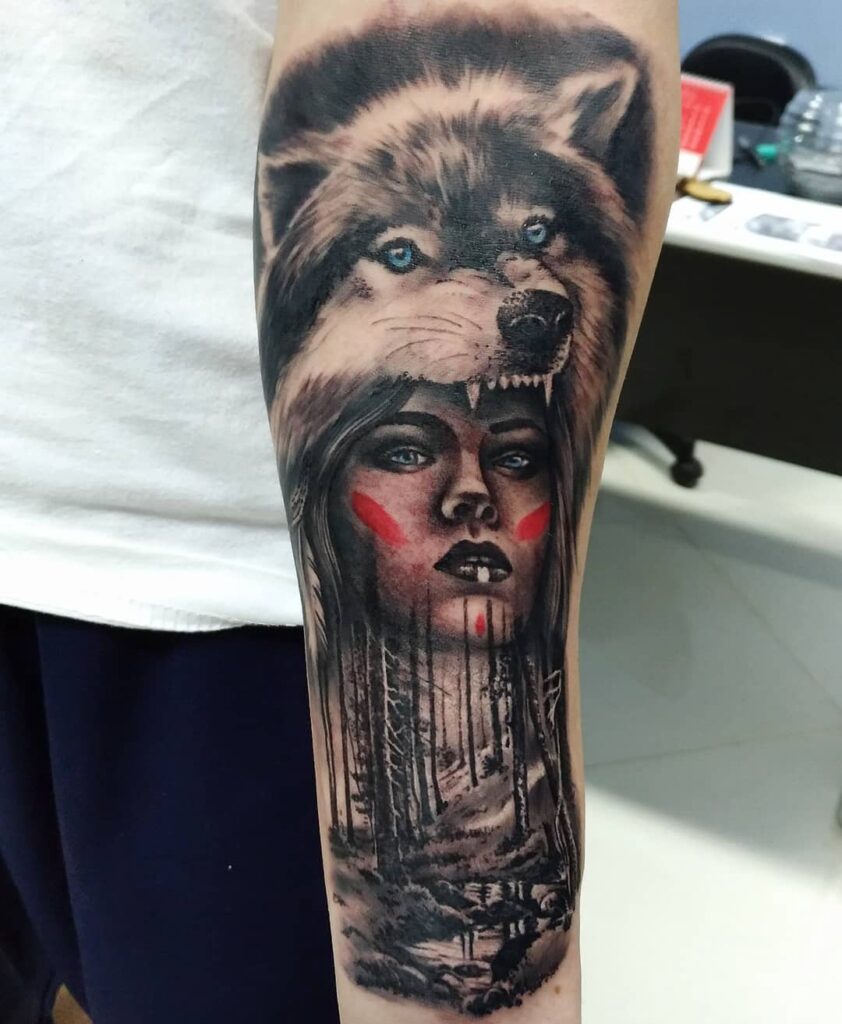 Tatuagem de braço com lobo, floresta e rosto feminino, transmitindo força e conexão com a natureza.
