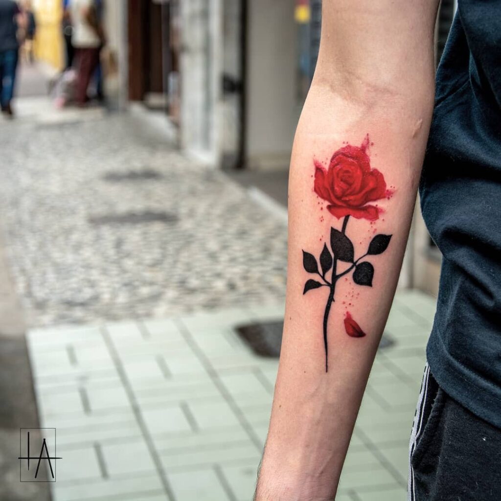 Tatuagem de rosa vermelha no antebraço em uma rua pavimentada.