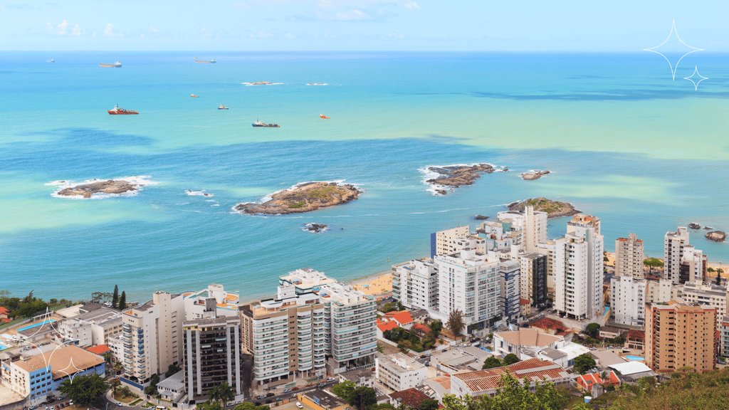 Vista aérea da costa com prédios modernos e barcos no mar esmeralda, mostrando um cenário urbano litorâneo vibrante.