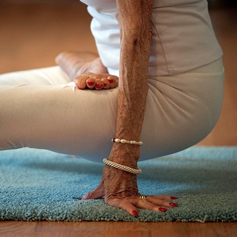 Pessoa praticando yoga com pulseiras no braço, em pose de equilíbrio sobre tapete azul.