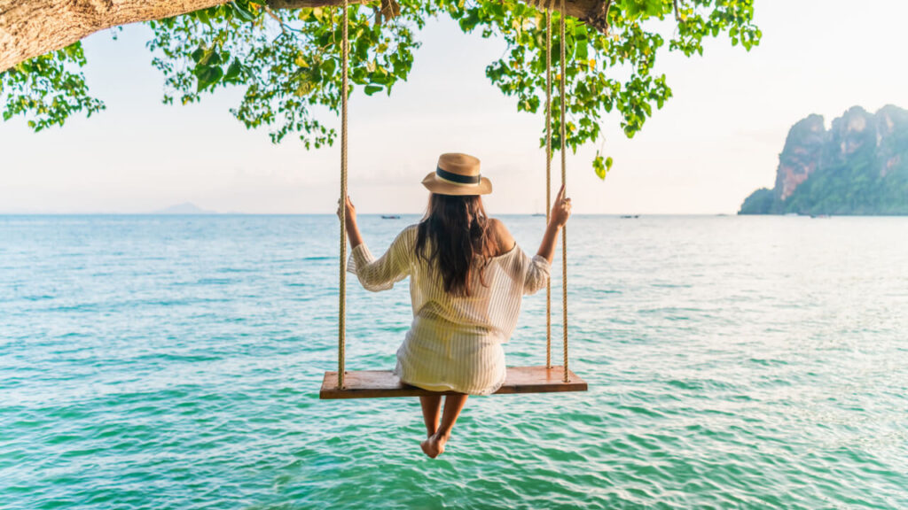 Mulher relaxando em um balanço acima de um mar. Conceito de sonho feliz.