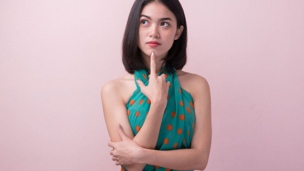 Mulher usando vestido casual, pensando em algo, isolada no fundo rosa.