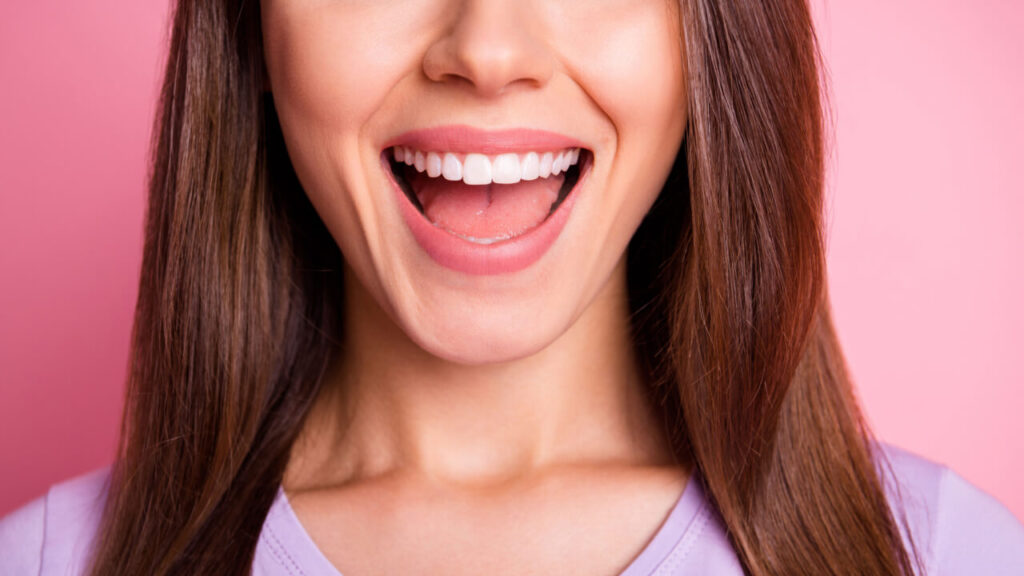 Retrato aproximado de uma mulher sorrindo com os dentes, isolada em um fundo rosa pastel.