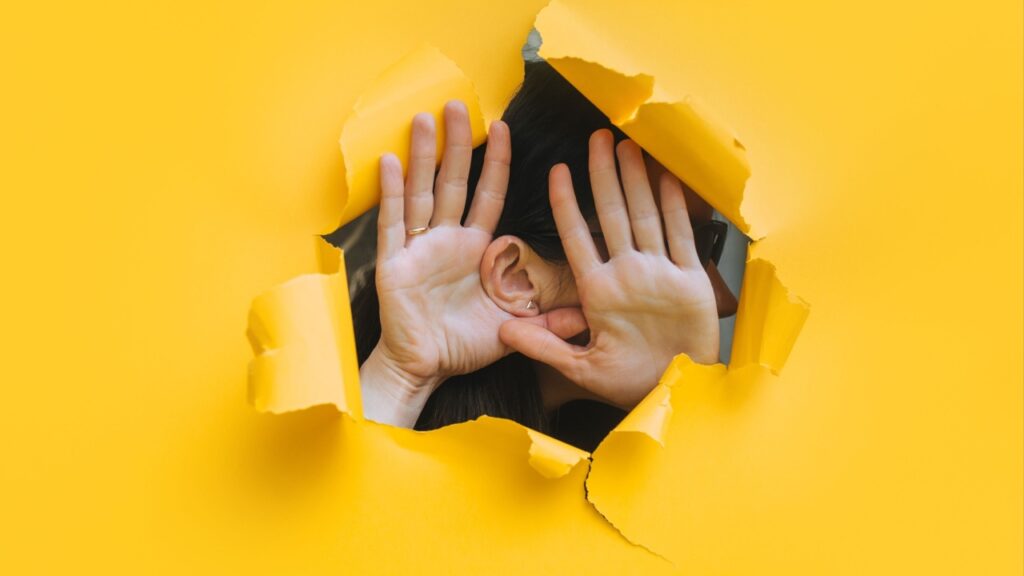 mulher ouvido através de uma parede amarelo com buraco no meio