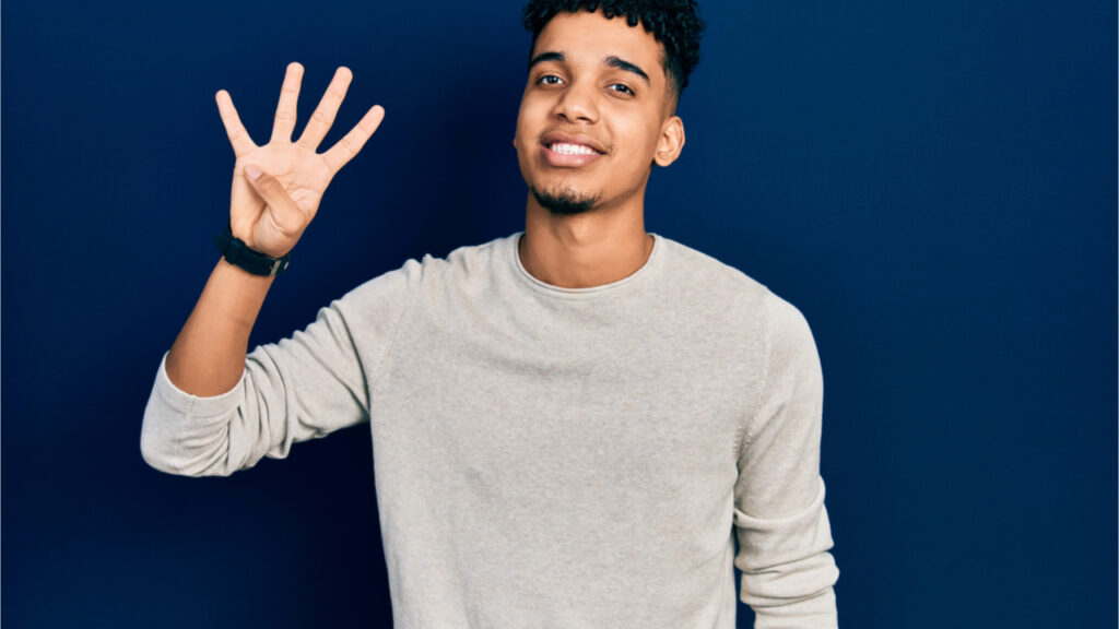 Jovem vestindo roupas casuais, mostrando e apontando para cima com os dedos em número 4, enquanto sorri confiante e feliz.