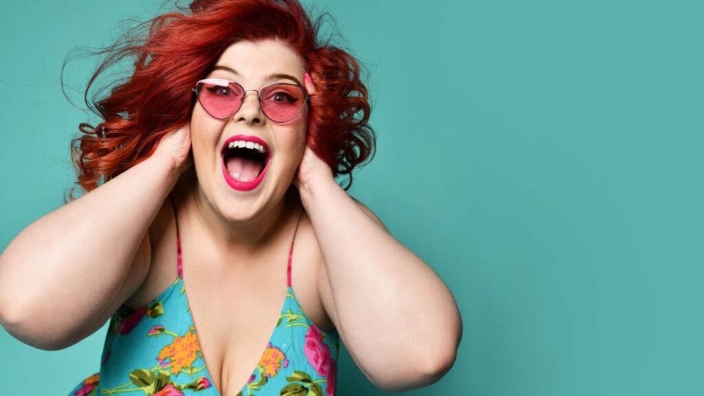 mulher de cabelo e óculos vermelhos com a boca aberta de felicidade em fundo verde água