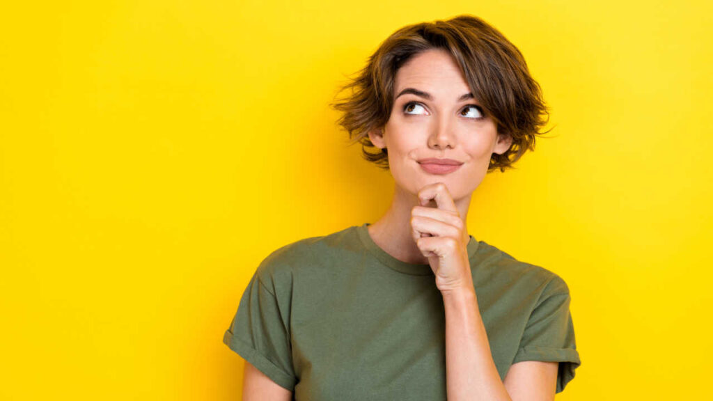 mulher com a mão no queixo em fundo amarelo