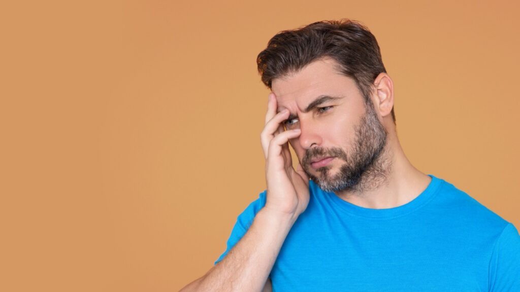 homem com expressão facial de irritado e mão no rosto em fundo marrom