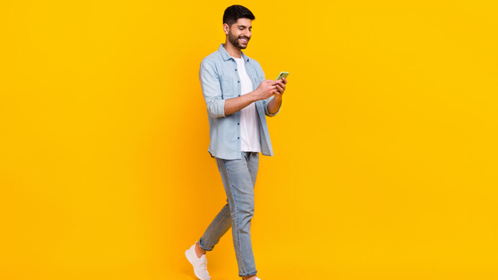 homem em pé mexendo no celular em fundo azul