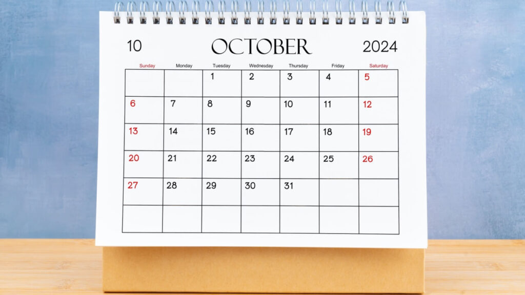 Calendário mensal de escritório para outubro de 2024 em uma mesa de madeira.