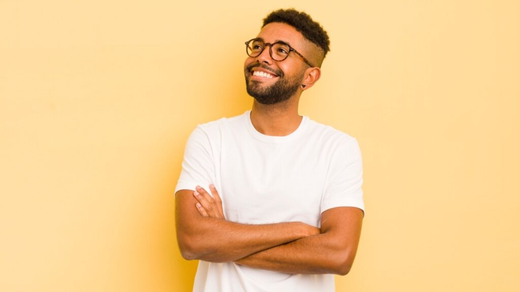 homem de braços cruzados sorrindo e olhando para cima em fundo laranja