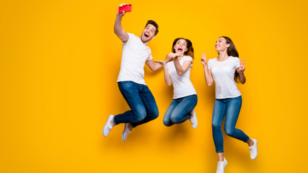 um homem e duas mulheres pulando em fundo laranja