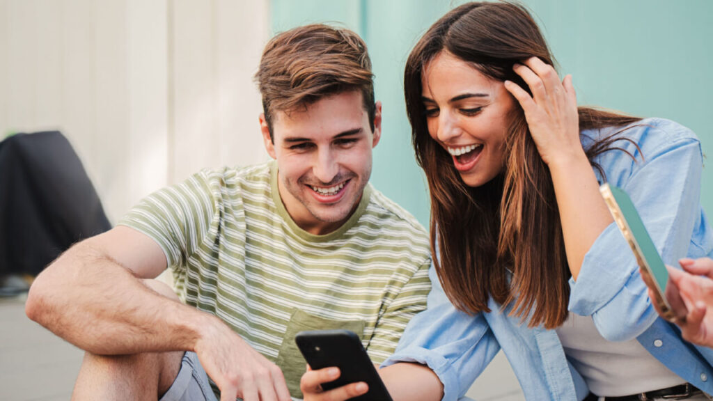 casal viajando em um ponto turístico com ela segurando um celular e os dois olhando para tela