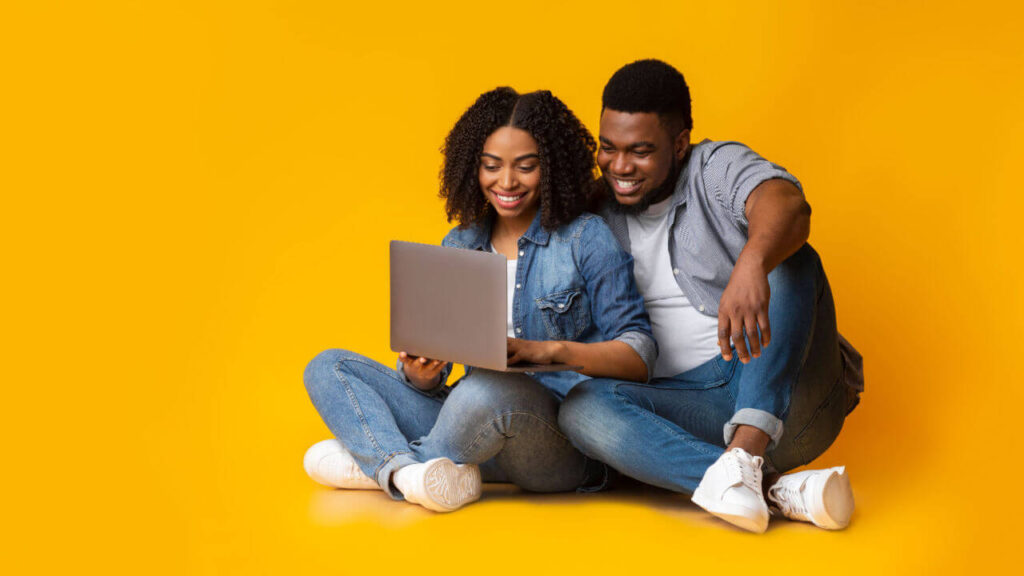 Jovens usando laptop enquanto estão sentados no chão sobre fundo amarelo no estúdio.