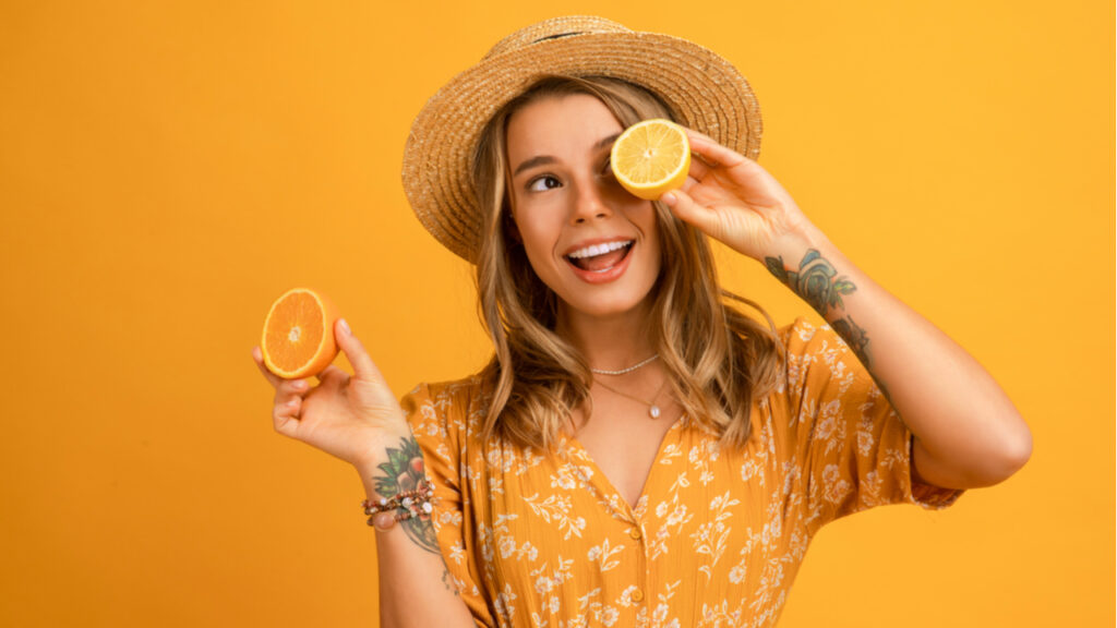 mulher com laranja na mão em fundo amarelo