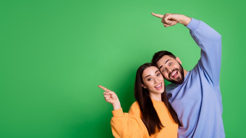 casal abraçados e com o braço direito levantado e apontando por lado em fundo verde