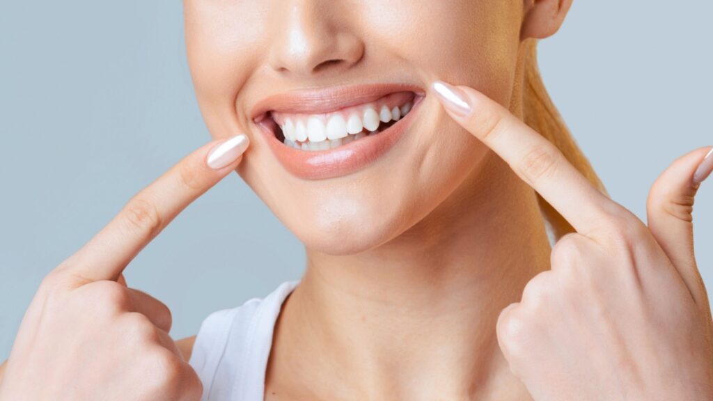 sorriso feminino sendo apontado por dois dedos indicadores em fundo azul