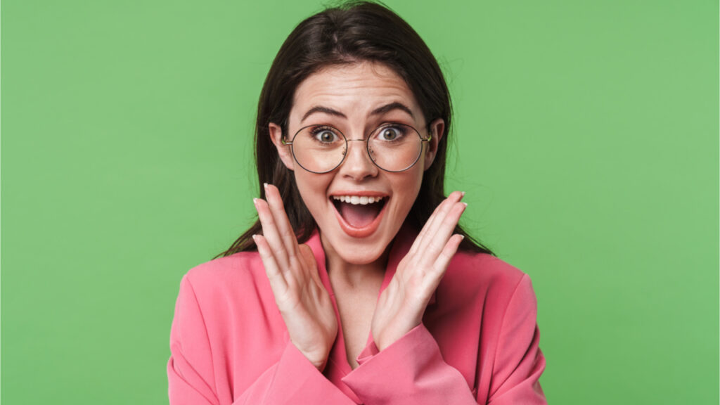 Retrato de uma jovem elegante e feliz, vestindo jaqueta rosa, isolada sobre fundo verde.