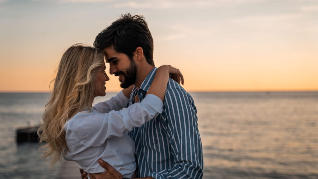 casal se abraçando com as testas coladas em uma praia ao pôr do sol