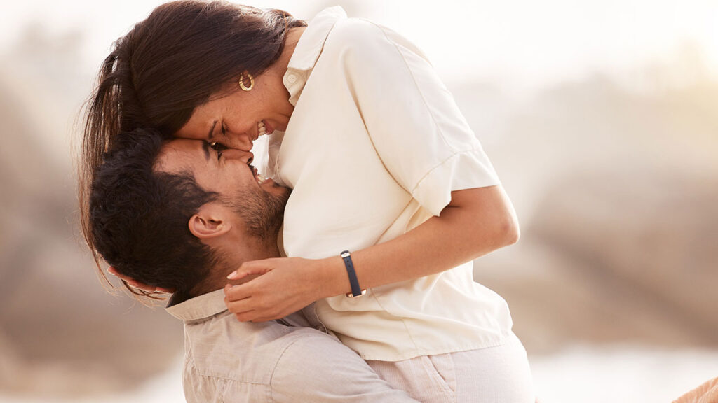 casal com a mulher abraçada no colo do homem e os dois sorrindo em um fundo ao ar livre