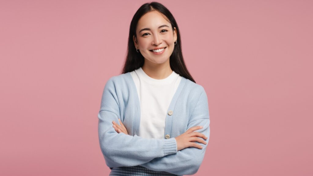 mulher de braço cruzado e sorrindo para a foto em fundo rosa