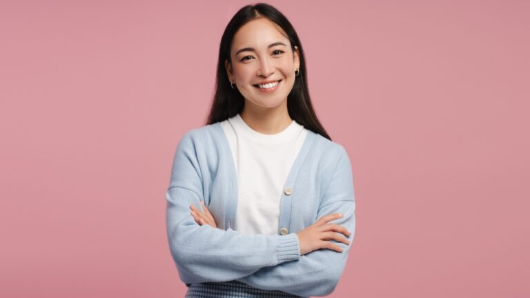 mulher de braço cruzado e sorrindo para a foto em fundo rosa