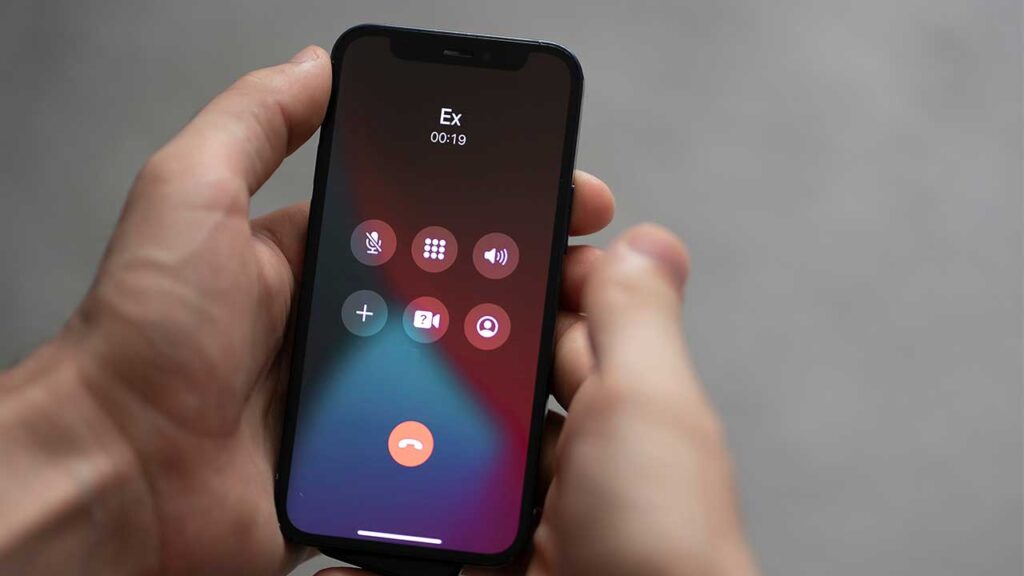 par de mãos segurando um celular onde a tela mostra a ligação de um ex em fundo cinza