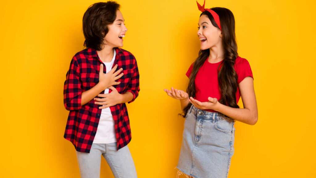 Foto de crianças alegres, conversando, olhando uma para a outra, rindo, isoladas em fundo de cor amarela.