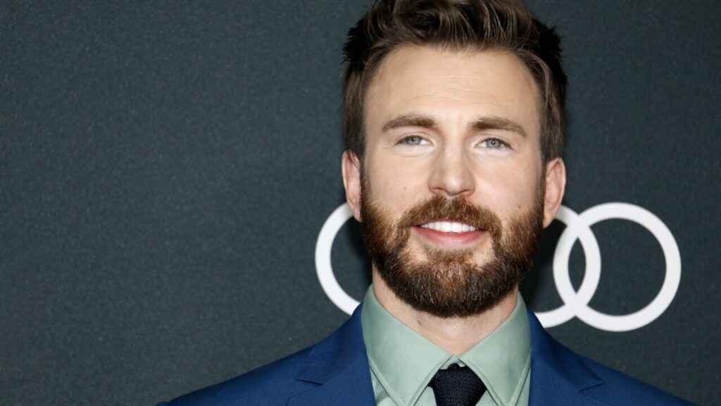 Ator Chris Evans sorrindo com um fundo preto