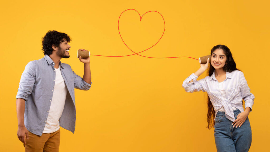 Mensagem de amor. Homem dizendo palavras românticas para namorada através de telefone de lata com corda em forma de coração, de pé sobre fundo amarelo.