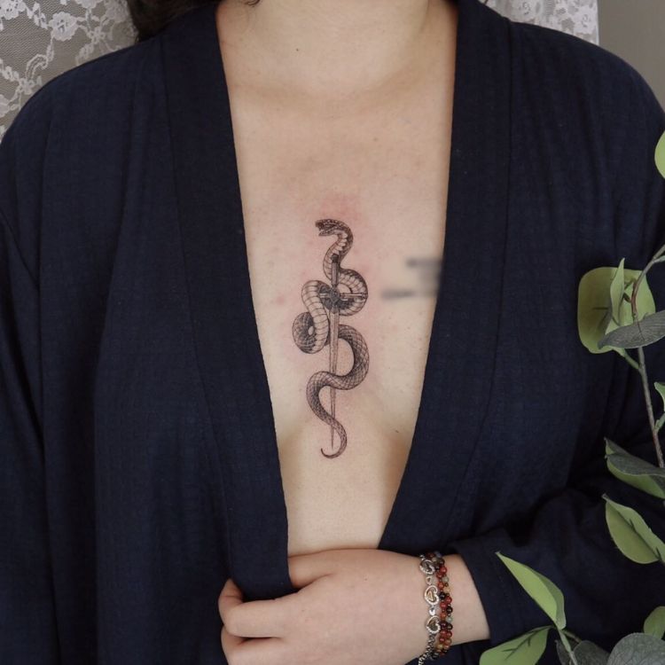 1-4 uma mulher com uma tatuagem entre os seios com uma espada e uma cobra