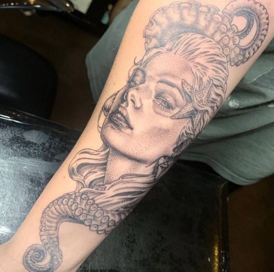 Foto de tattoo com o rosto da sereia no braço de uma mulher