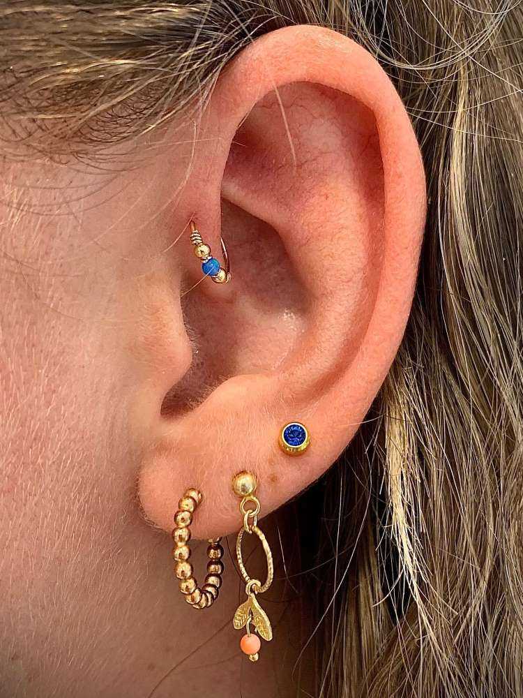 Orelha com três furos no lóbulo e argola no anti hélix, todas as joias em dourado e azul.