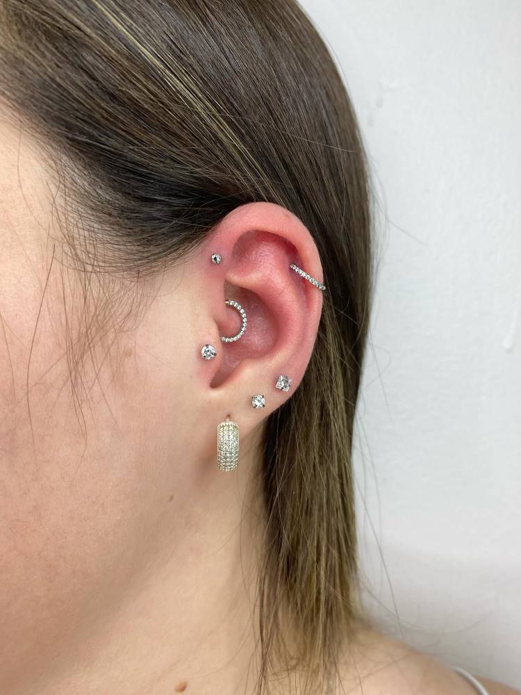 Orelha com lóbulo perfurado, assim como tragus, daith, hélix e anti hélix, tudo com zircônia