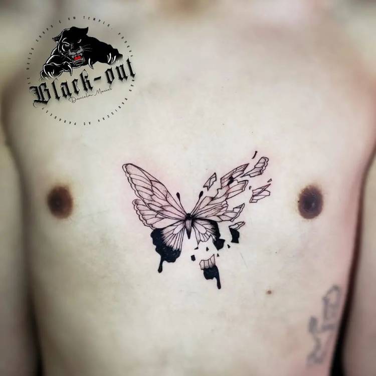asa-despedacada-peitoral-borboleta Tatuagem de borboleta no peitoral de um homem de pele clara. A borboleta é em traços pretos, sombreados e sua asa direita está estilhaçada.