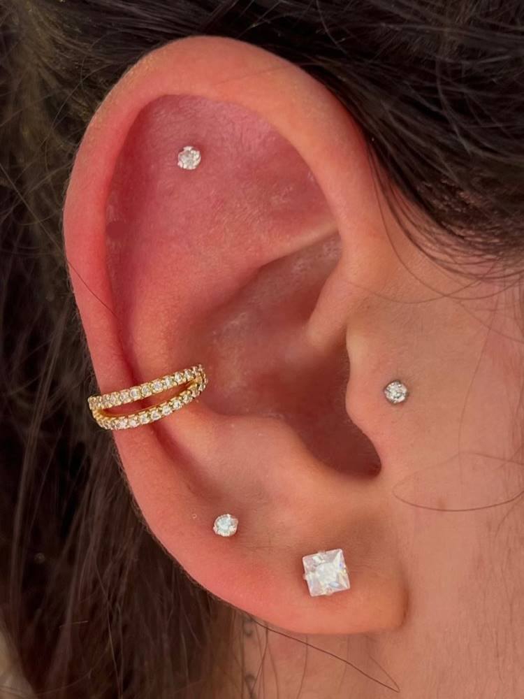Orelha com ponto de luz na scapha, tragus e lóbulo, além de um brinco quadrado no lóbulo e argola dourada no conch.