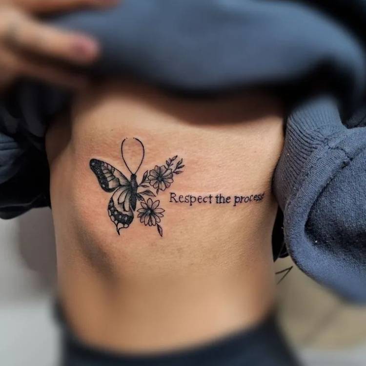 frase-flor-borboleta-costela Ttuagem grande de borboleta com traços finos e grossos, flores e frase "respect the process" na costela de uma mulher de pele clara.