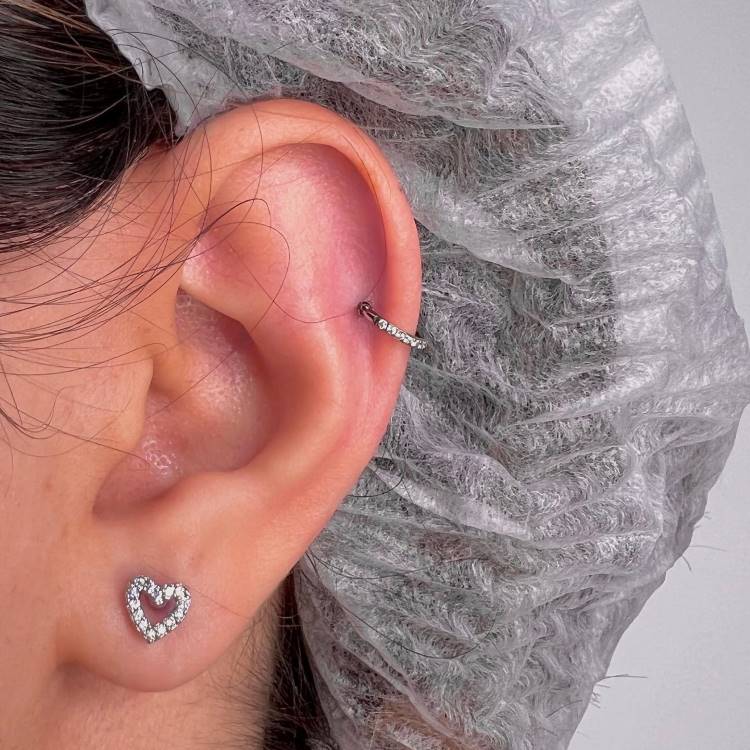 Orelha com brinco de coração com zircônia no lóbulo e argola no hélix.