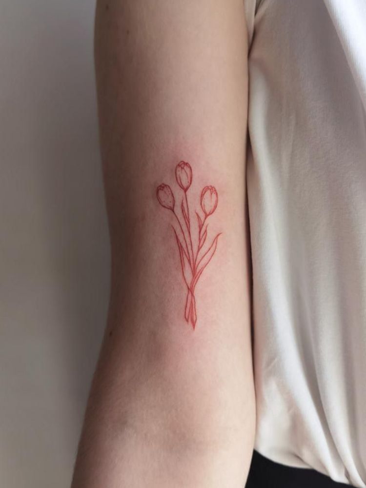 imagem-6-1 Foto de tatuagem no bíceps, com três tulipas em traço vermelho.