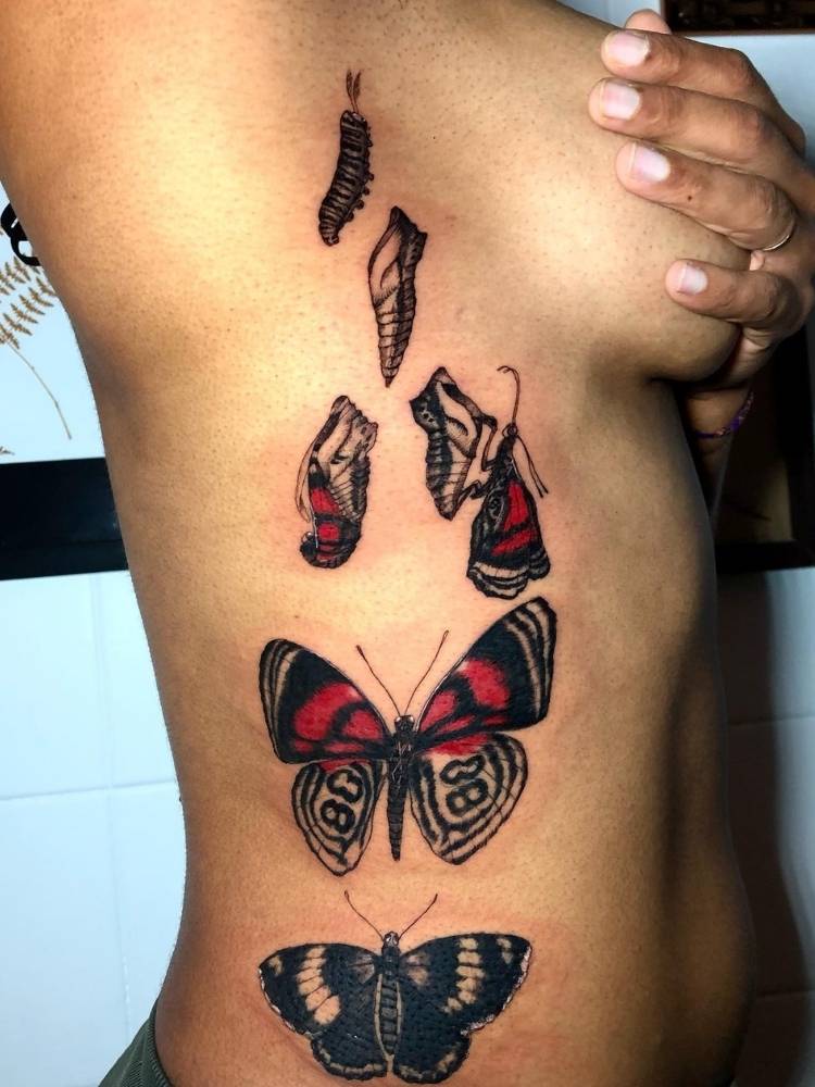 metamorfose-borboleta-costela Tatuagem grande na costela da metamorfose de uma borboleta. Próximo ao seio, há uma lagarta no casulo que vai se tornando borboleta conforme a tattoo se aproxima da cintura. A tatuagem é preta e vermelha, em estilo mais realista e feita em uma mulher de pele morena.