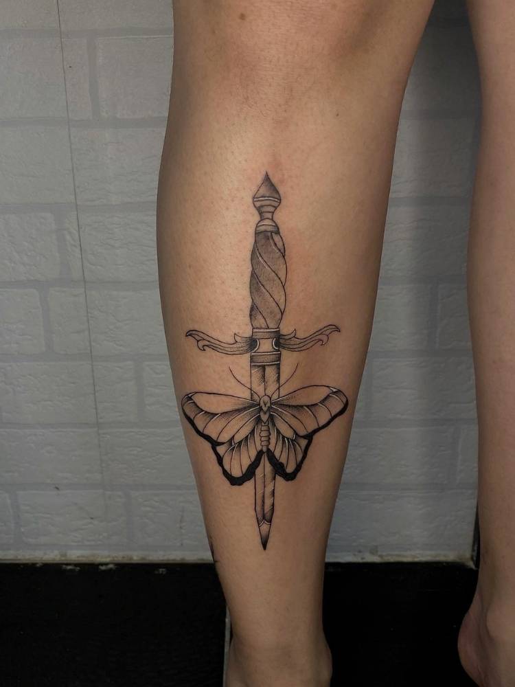 religiosidade-borboleta Tatuagem de borboleta com traços finos e grossos em uma perna de uma mulher de pele clara. A tattoo também apresenta uma adaga no meio da borboleta.