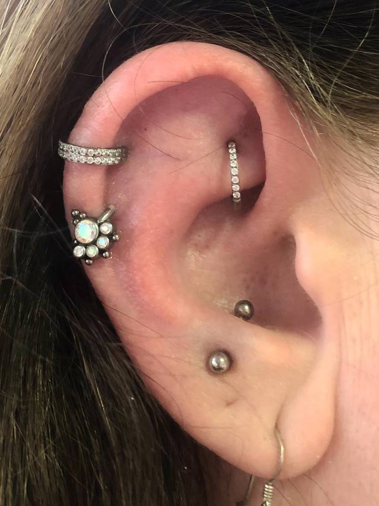 Orelha com piercing na hélix, rook e snug, tudo em prata.