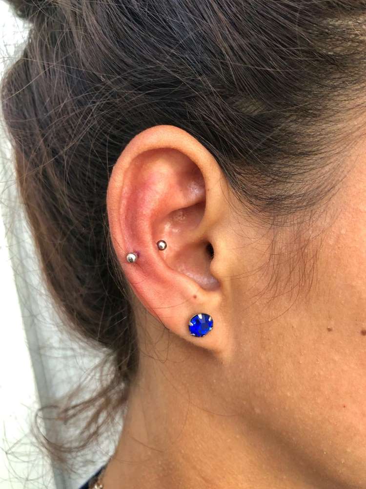 Orelha com piercing no slug e brinco azul no lóbulo.