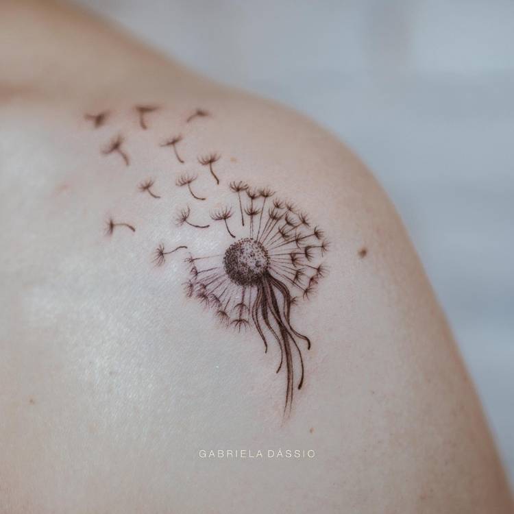 tatuagem-feminina-ombro-delicada-dente-leao Mulher de pele clara com ombro tatuado com dente de leão ao vento, em fine line e sombra