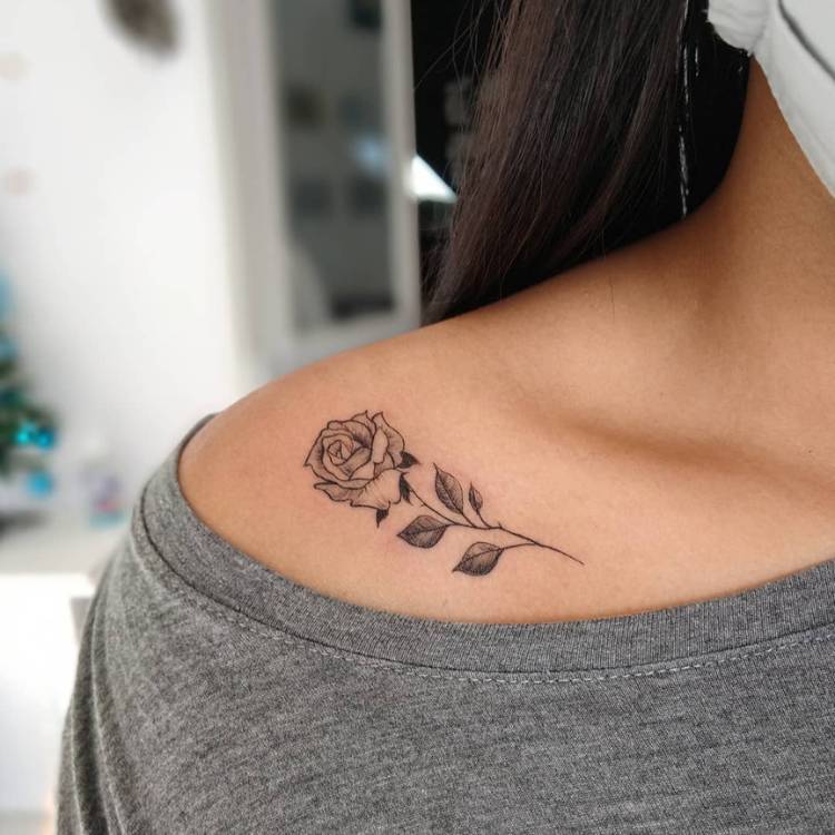 tatuagem-feminina-ombro-flor-delicada Mulher de pele morena e blusa cinza com rosa tatuada em preto estilo fine line no ombro