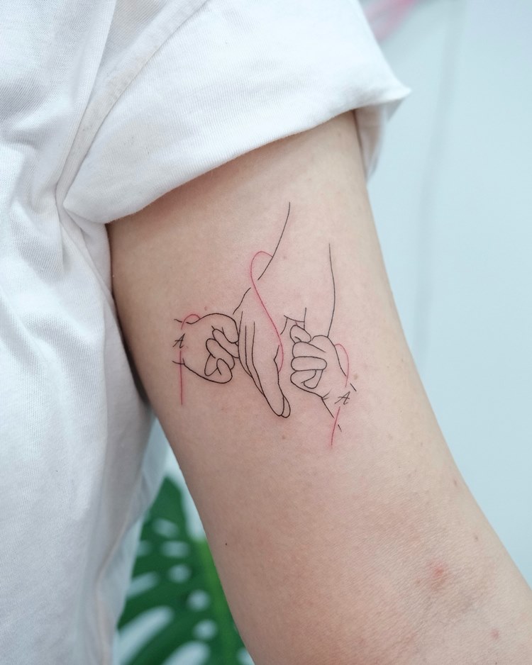 tatuagem-mae-para-filho Tattoo de mãe em homenagem aos filhos: traços finos: mão segurando as mãos dos filhos em volta de um fio vermelho. Tattoo no braço