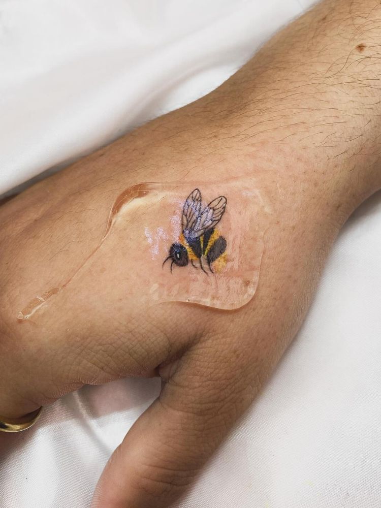 Mão com tatuagem de abelha colorida próxima ao dedão