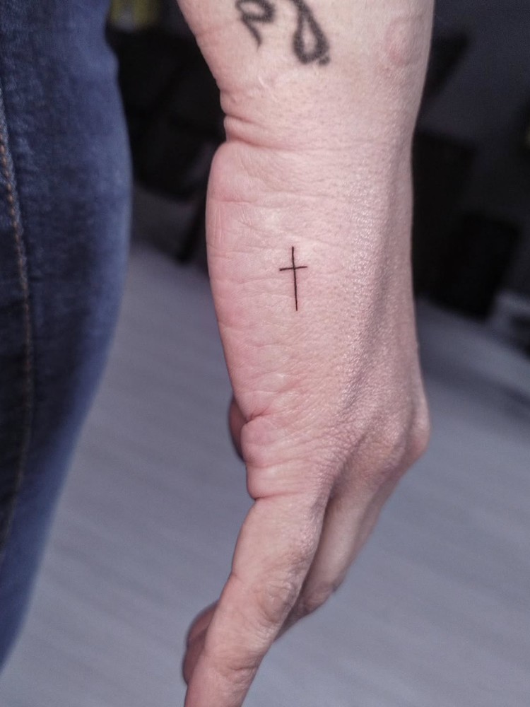Mão de lado com tattoo de cruz fineline na lateral